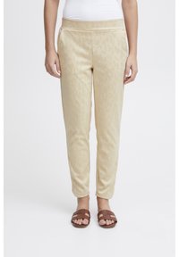 Jasnokremowe dresowe spodnie z delikatnym nadrukiem w panterkę, miękka textura, elastyczna talia i boczne kieszenie. Połączone z brązowymi klapkami.