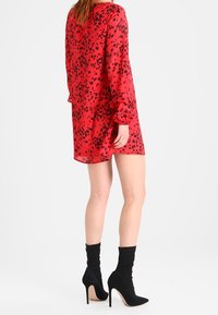 Rotes, durchsichtiges Kleid mit schwarzem Leopardenmuster, lange Ärmel mit Rüschen, knielang, kombiniert mit schwarzen Ankle-Boots auf Absätzen.
