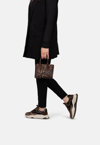 Borsa a tracolla con stampa leopardata marrone e manici corti. Top a maniche lunghe nero, gilet nero su misura e leggings neri. Sneakers marroni e nere.