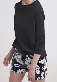 Chemise noire à manches longues avec un col rond, associée à un short à sequins présentant un motif floral en blanc et noir.