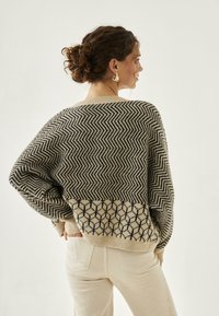 Jersey de punto en beige y negro con un patrón en forma de chevron en la parte superior y un diseño geométrico en la parte inferior. Corte holgado con hombros caídos.