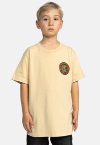 Licht beige korte mouwen t-shirt met een ronde hals en een kleurrijk grafisch logo op de borst. Zacht katoenen materiaal; ontspannen pasvorm.