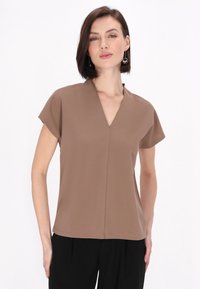 Top marrone a maniche corte con scollatura a V, realizzato in tessuto morbido. Presenta una vestibilità rilassata e un orlo senza cuciture, abbinato a pantaloni neri.