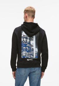 Sudadera negra con capucha que presenta una impresión fotográfica de rascacielos de la ciudad en azul y gris en la parte posterior, con puños y cintura acanalados.