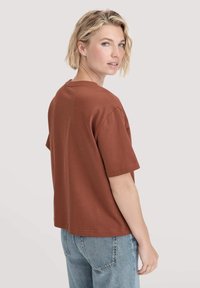 Bruine katoenen t-shirt met korte mouwen, ontspannen pasvorm, ronde halslijn en een subtiele textuur. Draag het met lichtblauwe denim jeans.