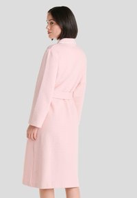Bata de tela de rizo rosa con un patrón texturizado de diamantes, mangas largas, cintura ajustable con cinturón y cuello tipo chal, que llega hasta la mitad de la pantorrilla.