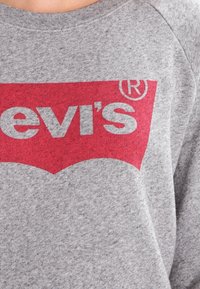 Felpa grigia con scollo rotondo, caratterizzata da un prominente logo rosso di Levi's sul petto, realizzata in tessuto morbido e testurizzato.