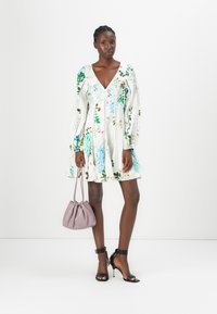 Abito bianco con stampa floreale, maniche lunghe a sbuffo, scollo a V, vita arricciata e dettagli all'orlo; abbinato a una borsa di colore viola chiaro e tacchi neri.