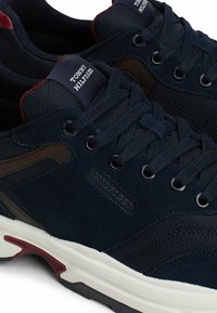 Granatowe sneakersy z siateczkowym i zamszowym wierzchem, z ciemnymi akcentami, okrągłymi sznurowadłami, metką z logo oraz białą podeszwą środkową z czerwonymi detalami.