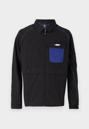 Black jacket featuring a blue mesh chest pocket, contrasting blue stitching, and snap buttons. Designed with a front zipper and long sleeves.