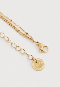 Guldfarvet kædedyse med lynlås og rund charme med indgraveringen "LIU·JO" samt dekorativ kant på hvid baggrund.