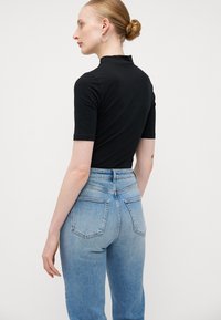 Top preto de manga curta com colarinho alto e design ajustado, emparelhado com jeans de cintura alta de cor azul clara, apresentando bolsos traseiros e detalhes costurados.