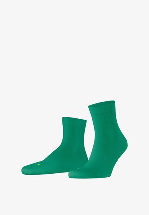 Chaussettes en coton vert avec des bords en côte et une texture lisse, présentant un bout arrondi et un subtil détail de marque jaune.