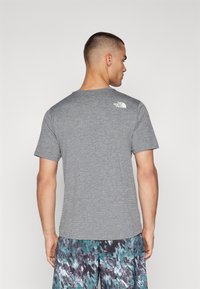 Camiseta gris de manga corta con cuello redondo y un pequeño logo blanco en la parte superior de la espalda, fabricada con un tejido texturizado.
