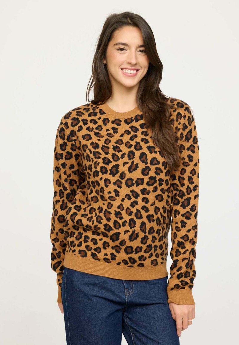 Pull en imprimé léopard marron avec des taches noires, col rond, manches longues et ourlet côtelé ; associé à un jean bleu. Matière en tricot douce.