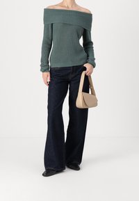 Maglione a spalle scoperte a coste color teal abbinato a jeans a gamba larga scuri e una borsa beige con design curvo e tracolla corta.