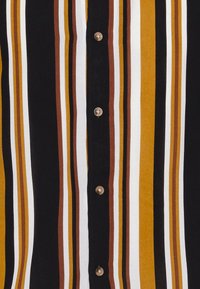 Camicia con bottoni, caratterizzata da righe verticali nere, bianche, gialle e marroni. Presenta bottoni rotondi dorati lungo il centro. Tessuto di morbida consistenza.