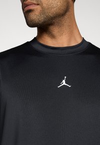 Μαύρο αθλητικό πουκάμισο από λείο ύφασμα, με στρογγυλή λαιμόκοψη και λευκό λογότυπο Jumpman στο κέντρο του στήθους.