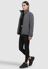 Gray quilted puffer jacket with high collar, diamond pattern, front zipper, and side pockets, worn over a black crop top and leggings.
