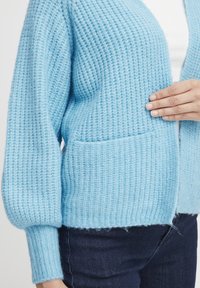 Cardigan lavorato a maglia azzurro chiaro con un motivo testurizzato, dotato di maniche ampie, una vestibilità comoda e una tasca frontale.