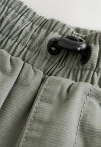 Licht olijfgroene shorts met een geraffineerde tailleband, voorzien van een zwarte trekkoord en fijne ribbels. Zichtbare stiksels accentueren de details.