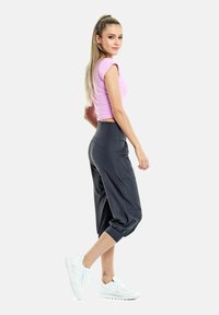 Pantaloni sportivi grigi a metà gamba con polsini elastici, abbinati a una maglietta aderente rosa a maniche corte e sneakers bianche.
