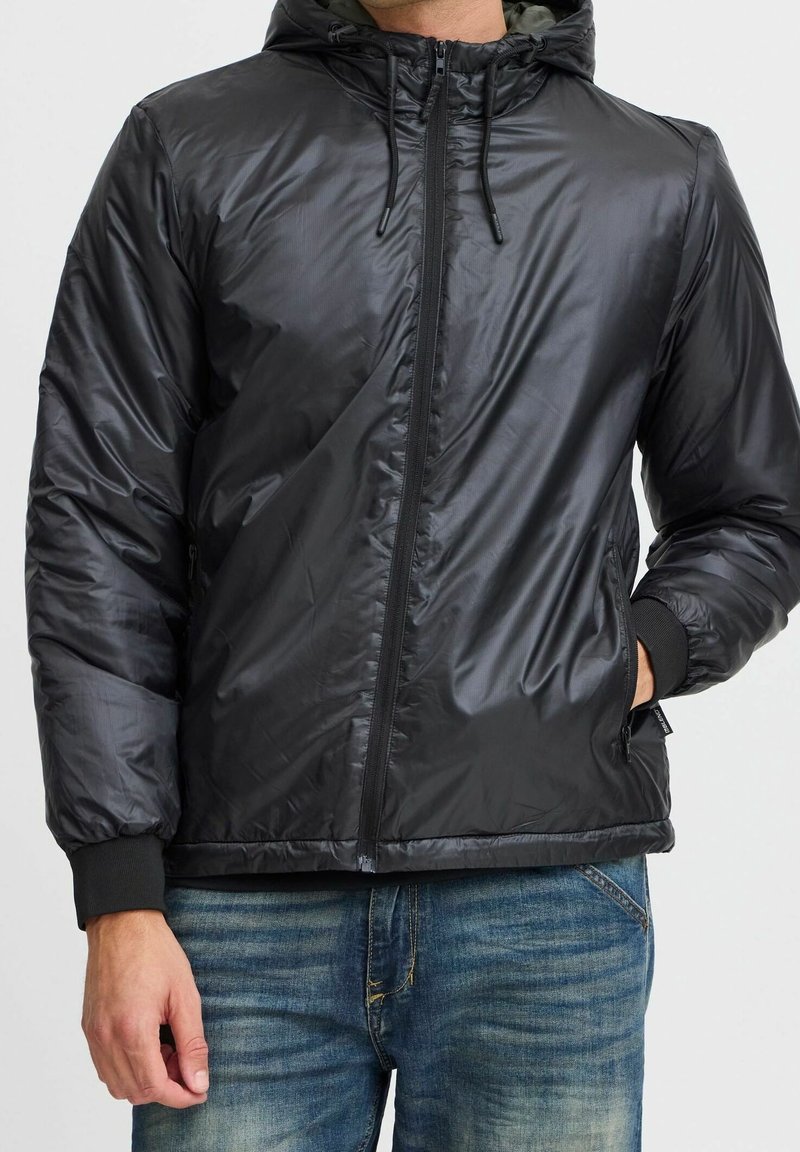 Schwarze, leichte Steppjacke mit Kapuze, Reißverschluss, gerippten Bündchen und Seitentaschen. Glatte Textur und glänzendes Finish.