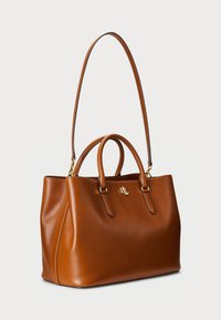 Brown leather tote bag with dual handles, long adjustable strap, gold-tone hardware, and embossed logo. Smooth texture, structured design.