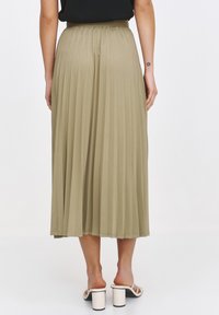 Plisowana spódnica midi w oliwkowym kolorze z elastycznym paskiem w talii. Miękki materiał swobodnie opada do połowy łydki. Noszona z kremowymi sandałami na słupku.