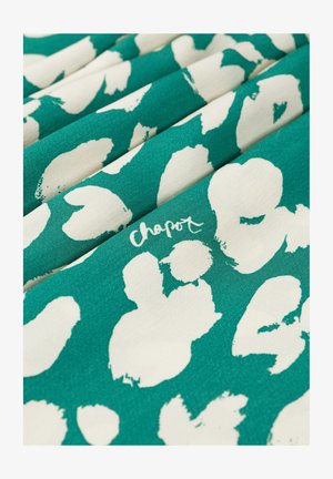 Turkooise stof met grote onregelmatige witte bloemmotieven en "chapot" handgeschreven tekst zichtbaar op de plooien.