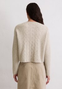 Beiger, kabelgestrickter Pullover mit kurzem Schnitt, langen Ärmeln und strukturiertem Muster, kombiniert mit einem hellbeigen Rock.