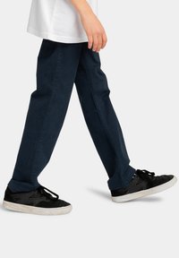 Zwarte sneakers met witte zolen, marineblauwe broek met een rechte snit en een wit T-shirt. De broek heeft een gladde textuur en geen zichtbare patronen.