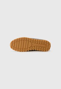 Sole of a shoe with a textured rubber surface, featuring a zigzag pattern and grooves for traction, in brown color.