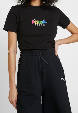 Personne portant un t-shirt de sport Puma noir avec un logo coloré et un pantalon de sport Puma noir avec une taille à cordon et un logo blanc sur la jambe gauche.