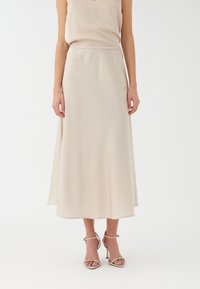 Una falda midi de suave y ligero tejido beige con un diseño fluido, que cuenta con una cintura elástica y un sutil brillo. Los tacones de aguja complementan el conjunto.