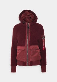 Bordó bunda s měkkou texturou, prošívaným vnitřkem, zipovým zapínáním, dvěma předními kapsami a nastavitelnou kapucí. Obsahuje boční kapsu s akcentem.