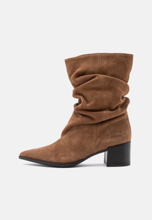 Brauner Wildleder-Mittelschaftstiefel mit nachgiebiger Passform, spitzer Zehenpartie und Blockabsatz, mit dezentem Branding an der Seite.