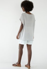 Lekki sweter z dzianiny w poziome beżowe i białe paski, z krótkimi rękawami i luźnym krojem, w połączeniu z jasnymi szortami i sandałami.