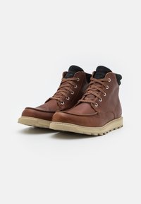 Bottes chelsea en cuir marron avec des côtés structurés, semelles en caoutchouc beige et doublure en tissu noir contrastant en haut. Design à lacets avec œillets en métal.