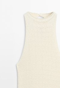 Close-up of sleeveless cream knitted top with high neckline and small button closure at back.
