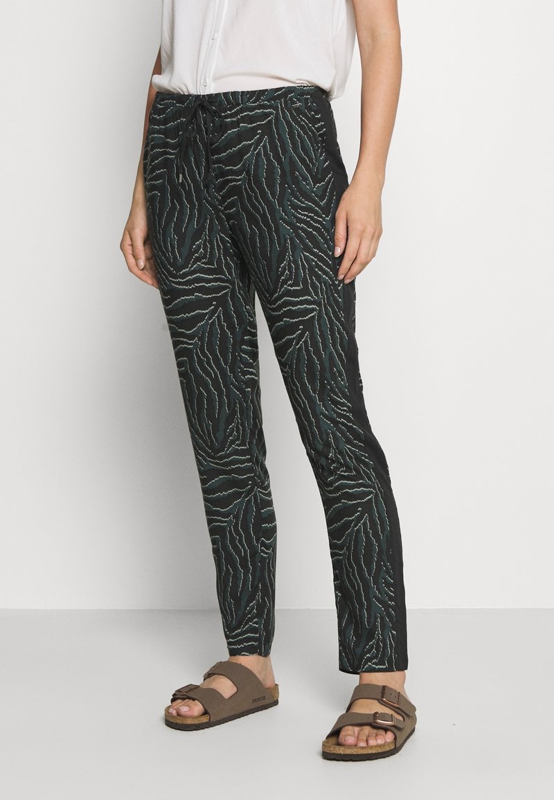 Personne portant un pantalon slim à motifs noirs et blancs, un chemisier blanc à manches courtes et des sandales marron avec boucles.