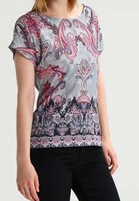 Kortärmad blus i grått med ett färgglatt paisleymönster, med intrikata detaljer i rosa och mörkblått, slät textur.