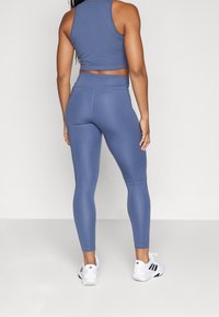 Idrottskläder i dämpad blå färg, bestående av en figurnära crop top och högmidjade tights, båda i slät tyg. Bärs tillsammans med vita sportskor.