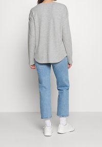 Grå, langærmet trøje med rundt kant, parret med lysblå, lige ben jeans og hvide sneakers. Blød, afslappet stof tekstur.