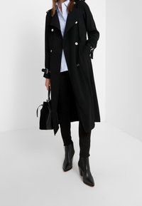 Abrigo negro con diseño de doble botonadura, botones plateados y puños ajustables. Combinado con una camisa azul claro, pantalones negros y botas de tacón.