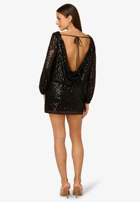 Czarna mini sukienka z cekinami, z długimi rękawami i głębokim dekoltem na plecach, z drapowanym fasonem i akcentem w postaci związania z tyłu.