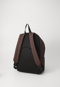 Backpack in dark brown fabric with mesh back, padded straps, and structured shape. Notable features include adjustable buckles and textured panels.
