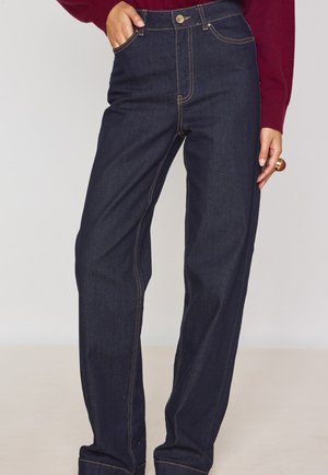 Jeans high-waisted blu scuro con gambe dritte, cuciture arancioni a contrasto, cinque tasche e chiusura con bottone metallico.