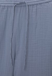 Ljust blå vävda byxor med elastisk midja och dragsko. Tyget har en texturerad, krinklad yta.