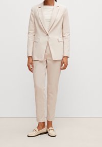 Jasnoróżowy garnitur z dopasowaną marynarką i prostymi spodniami, zestawiony z jasną koszulą w paski i kremowymi mokasynami z ozdobnym okuciem.